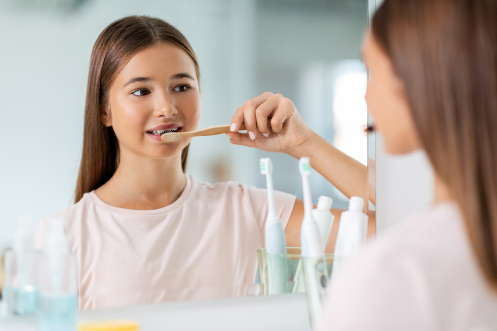 smiling teenage girl with toothbrush brushing teeth