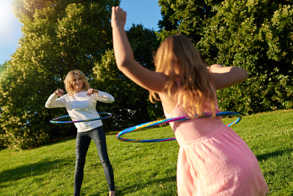 Mother and young daughter playing with hula hoops outside