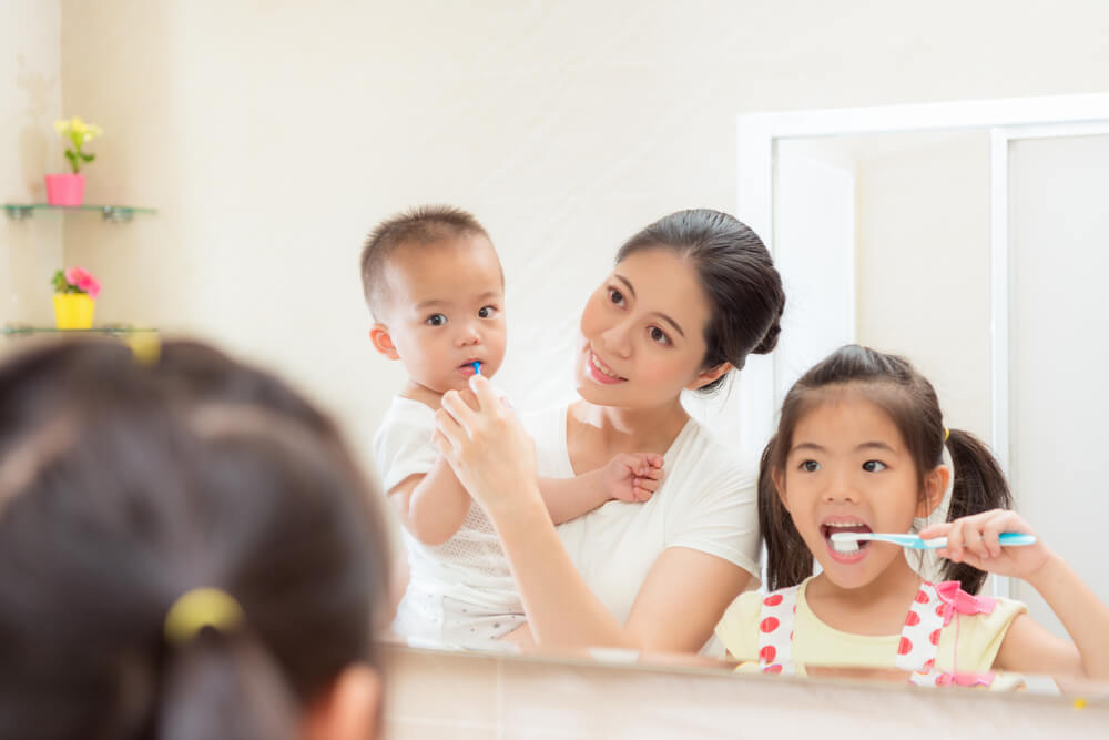 mom holding little baby son using toothbrush cleaning his teeth